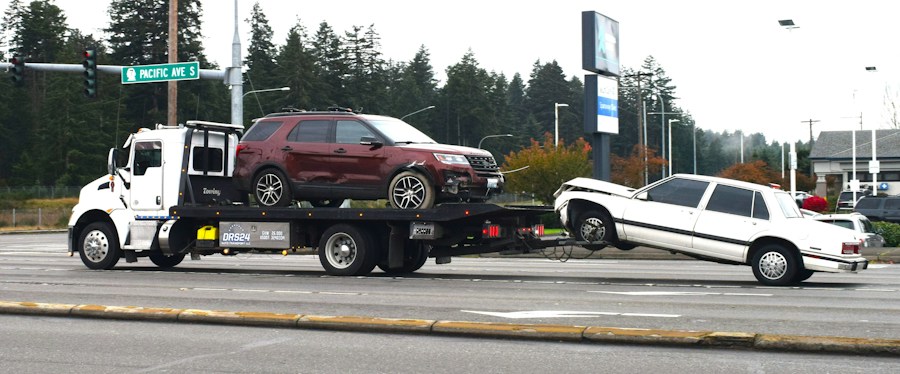 A tow truck carrying a damaged car away from a crash